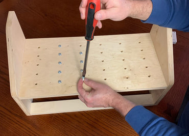 Person using a screwdriver to assemble screws on a wooden surface